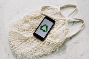 A phone with the recycle symbol displayed on it sits atop a mesh market bag. 